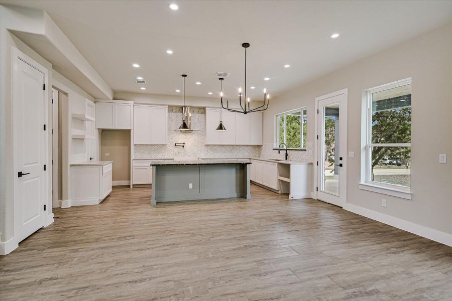 Two tone kitchen with suspended lighting, a kitchen island with sink, light wood-type flooring, tasteful backsplash, and open floor plan