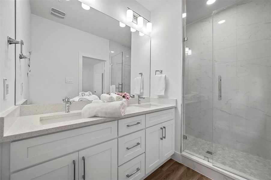 Full bath with double vanity, a sink, a marble finish shower, and wood finished floors