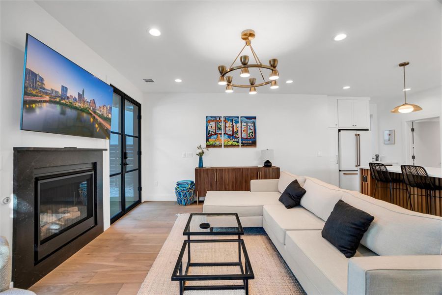 Living room with recessed lighting, light wood-style flooring, a glass covered fireplace, and a chandelier Living room with recessed lighting, light wood-style flooring, a glass covered fireplace, and a chandelier