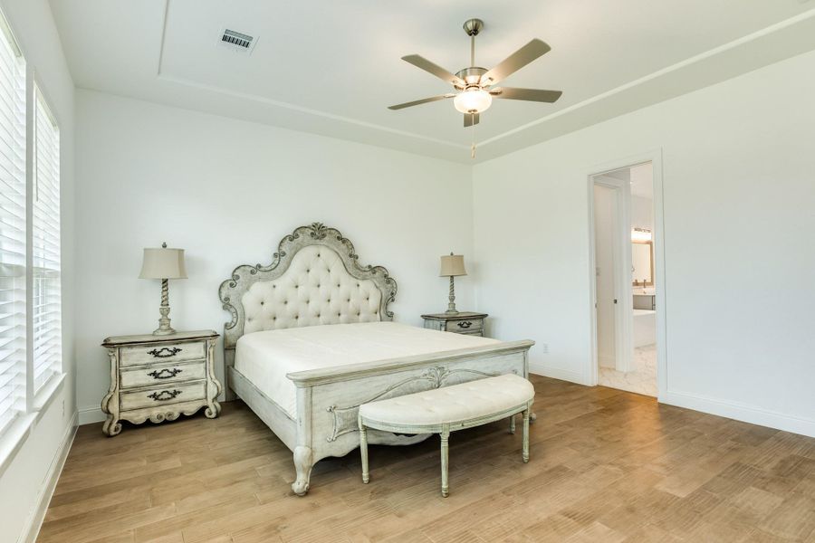 The primary suite is situated off the family room, offering total privacy. This space features elegant hardwood flooring, a high ceiling with an integrated fan, and a scenic view of the backyard.