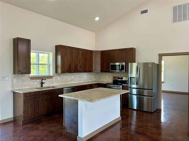 Kitchen featuring decorative backsplash, stainless steel appliances, concrete flooring, light stone countertops, and high vaulted ceiling