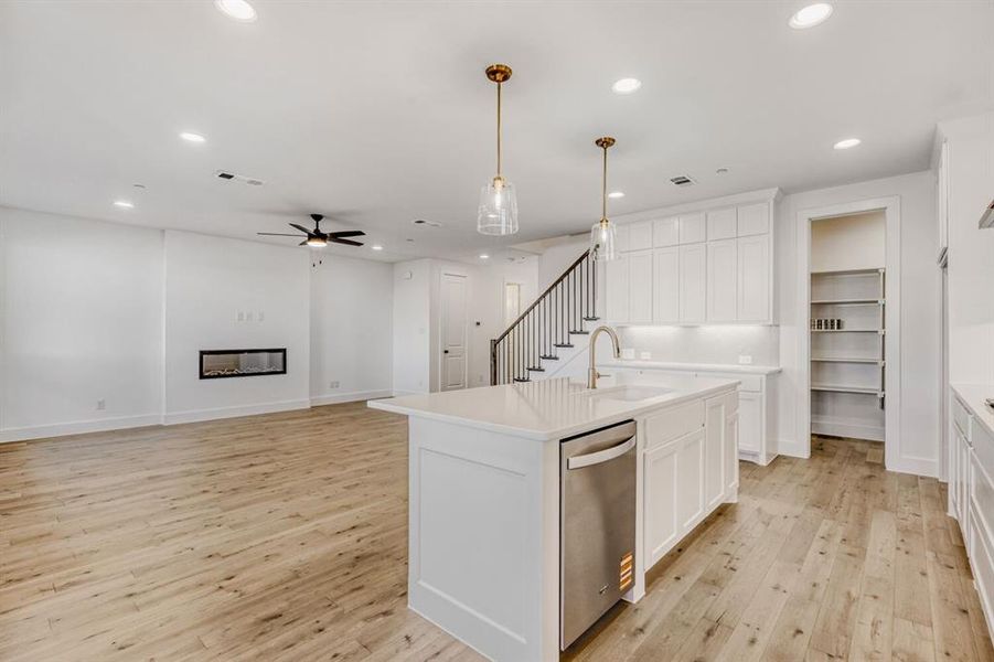 Kitchen featuring a kitchen island with sink, open floor plan, stainless steel dishwasher, a glass covered fireplace, and white cabinetry