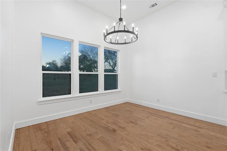 Unfurnished dining area with hanging lights, wood finished floors, and a high ceiling