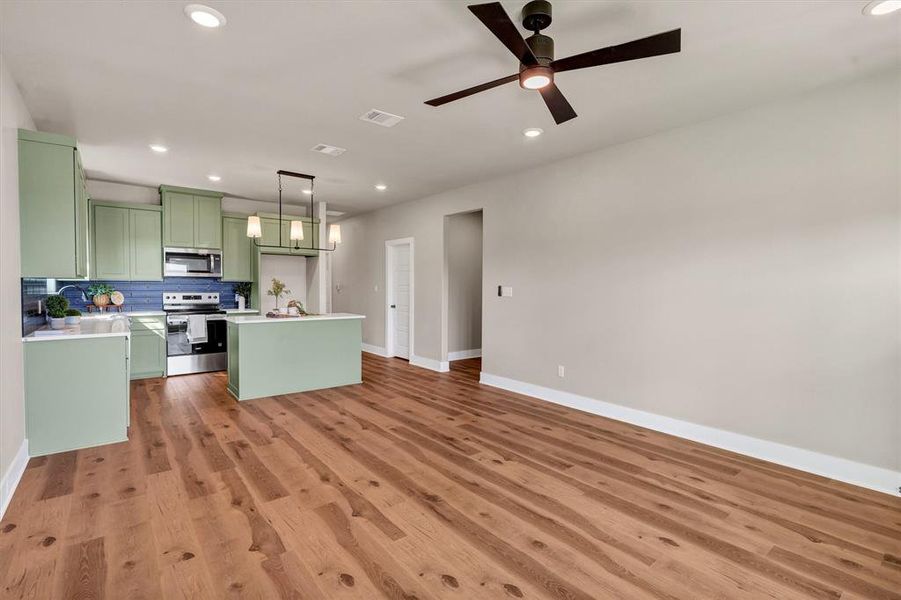 Kitchen with green cabinetry, decorative backsplash, a center island, light countertops, and stainless steel appliances Kitchen with green cabinetry, decorative backsplash, a center island, light countertops, and stainless steel appliances
