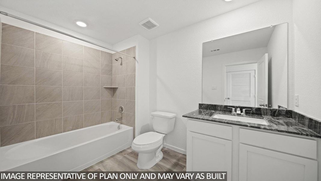 Bathroom featuring a tiled tub-shower combination with an integrated shelf, a white toilet, and a vanity with a dark patterned countertop, an integrated sink, a chrome faucet, and a large wall-mounted mirror