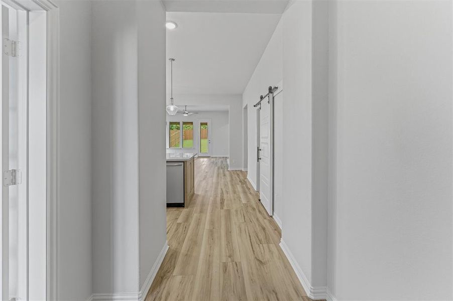 Expansive hall featuring wood-finish flooring, white walls, and a barn door leading to an interior space