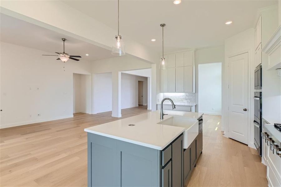 Kitchen with backsplash, a center island with sink, white cabinetry, and ceiling fan