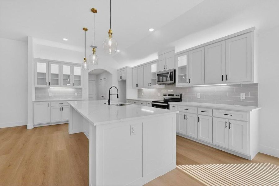 Kitchen featuring glass insert cabinets, arched walkways, white cabinets, and decorative light fixtures