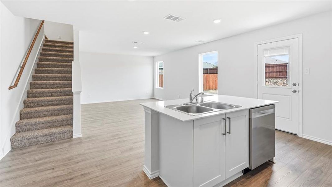Kitchen with light countertops, a center island with sink, light wood-style floors, stainless steel dishwasher, and open floor plan