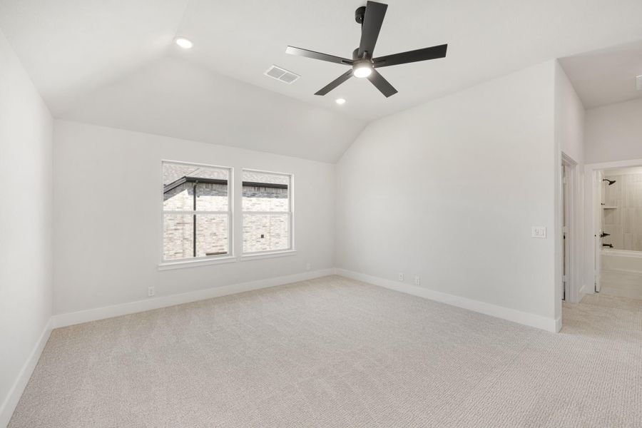 Empty bedroom with vaulted ceiling, black ceiling fan, carpet flooring, and ensuite bathroom doorway visible.