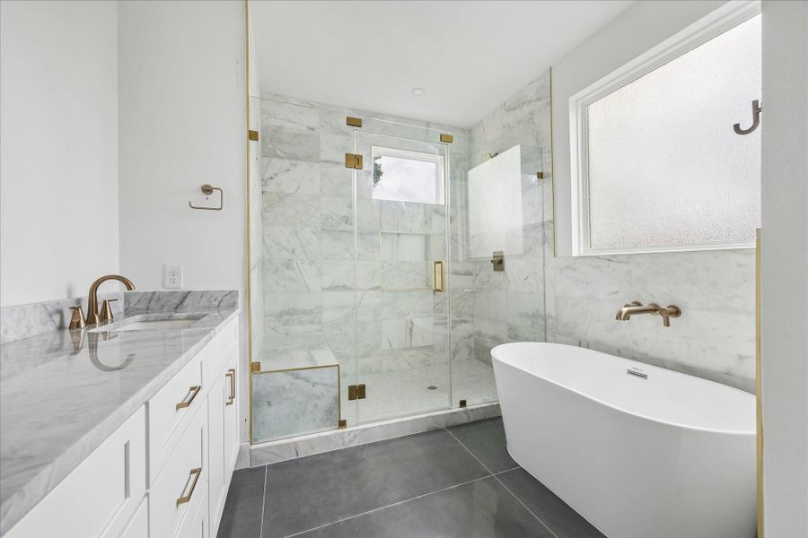 Spa-like primary bath with a luxurious soaking tub, glass-enclosed shower with bench seating, dual sinks, and dolomite countertops.