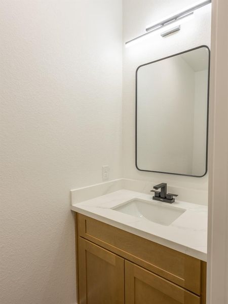 Tucked away for privacy, the powder bath offers a sleek quartz countertop, warm wood vanity, and bold matte black fixtures—perfect for guests. Tucked away for privacy, the powder bath offers a sleek quartz countertop, warm wood vanity, and bold matte black fixtures—perfect for guests.