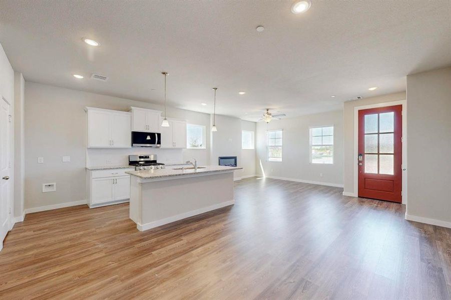 Kitchen with pendant lighting, an island with sink, open floor plan, white cabinetry, and appliances with stainless steel finishes