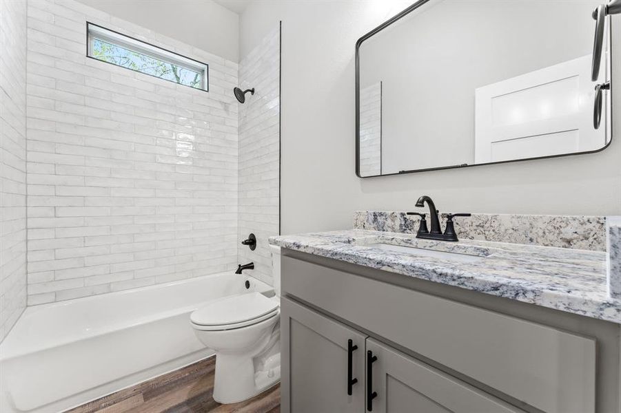 Full bathroom with tiled shower / bath, toilet, vanity, and wood-type flooring