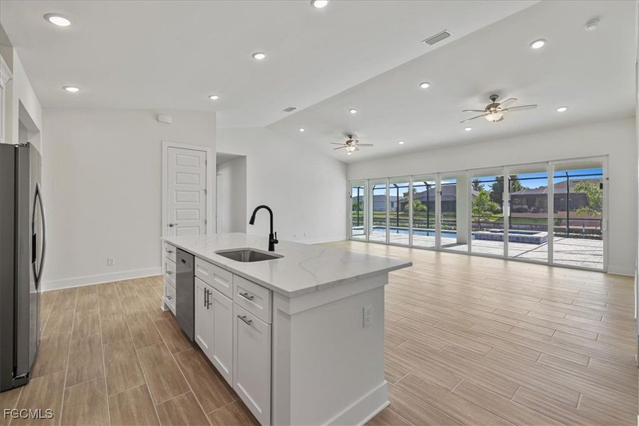 Kitchen featuring lofted ceiling, open floor plan, white cabinetry, appliances with stainless steel finishes, and light stone counters
