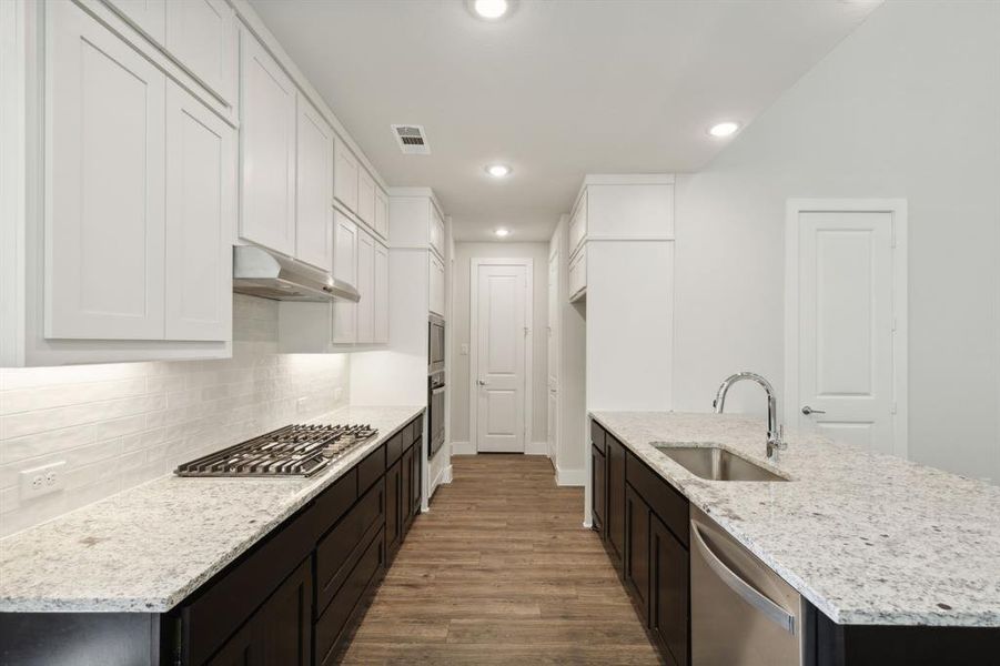 Kitchen with visible vents, wood finished floors, stainless steel appliances, under cabinet range hood, and a sink