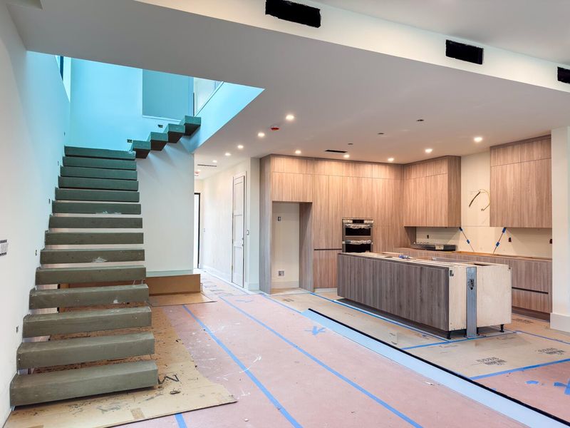 (as of April 8, 2026) a gorgeous floating concrete staircase anchors the living area under a double-height ceiling, glass railings are in the process of being installed