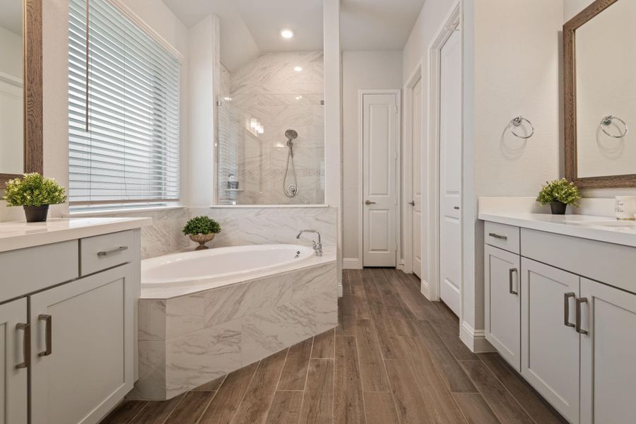 This bathroom features a spacious layout with a luxurious corner bathtub surrounded by elegant marble tiling. It has stylish wood-look flooring, dual vanities with ample storage, and modern fixtures. Natural light streams through a large window with blinds, creating a bright and inviting atmosphere. This bathroom features a spacious layout with a luxurious corner bathtub surrounded by elegant marble tiling. It has stylish wood-look flooring, dual vanities with ample storage, and modern fixtures. Natural light streams through a large window with blinds, creating a bright and inviting atmosphere.