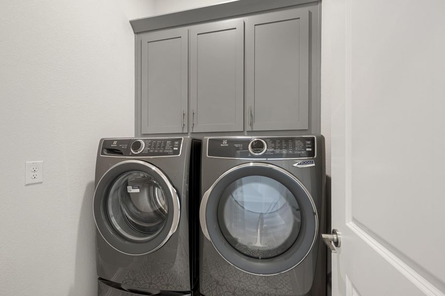 Laundry room with front-load washer and dryer set below gray upper cabinets Laundry room with front-load washer and dryer set below gray upper cabinets