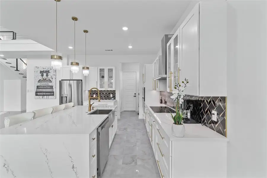 Spacious modern kitchen featuring a large kitchen island with a built-in sink, white cabinetry with gold-tone hardware, and a striking black and gold-tone backsplash