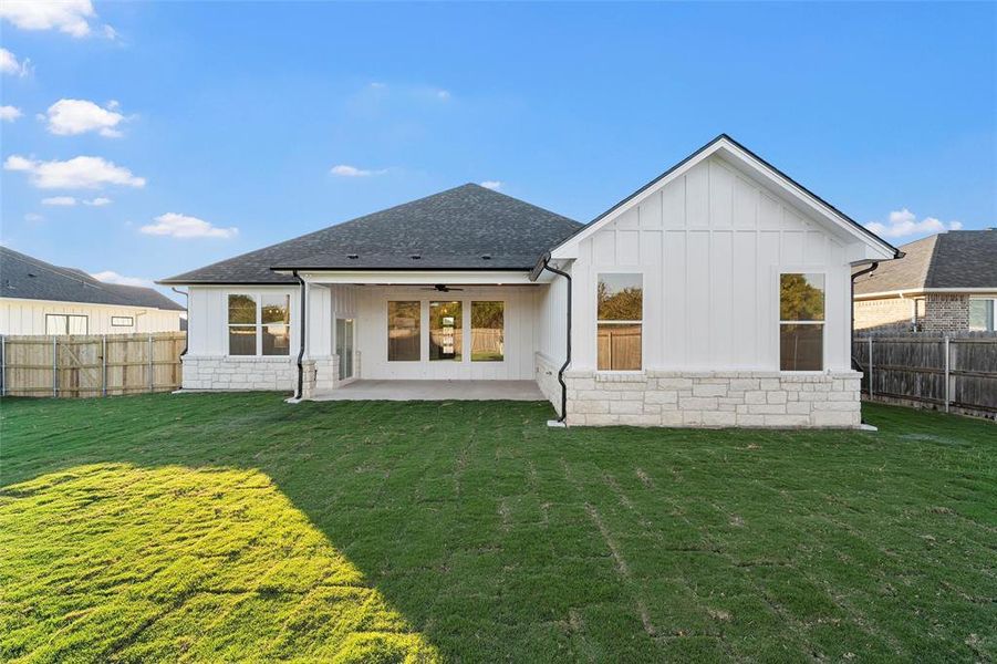 Back of property with a fenced backyard, board and batten siding, a patio, ceiling fan, and roof with shingles