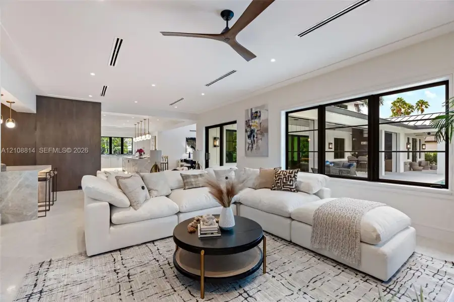 Open-concept living space featuring high ceilings with recessed lighting, a modern ceiling fan, expansive black-framed windows, and light-toned flooring Open-concept living space featuring high ceilings with recessed lighting, a modern ceiling fan, expansive black-framed windows, and light-toned flooring