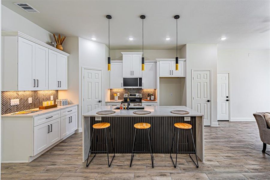 Kitchen with light stone countertops, an island with sink, light wood-style flooring, white cabinets, and recessed lighting