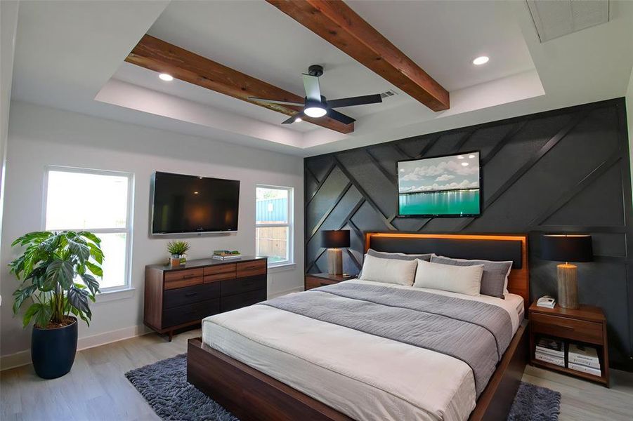 Bedroom featuring light wood-style flooring, multiple windows, beamed ceiling, ceiling fan, and a raised ceiling Bedroom featuring light wood-style flooring, multiple windows, beamed ceiling, ceiling fan, and a raised ceiling