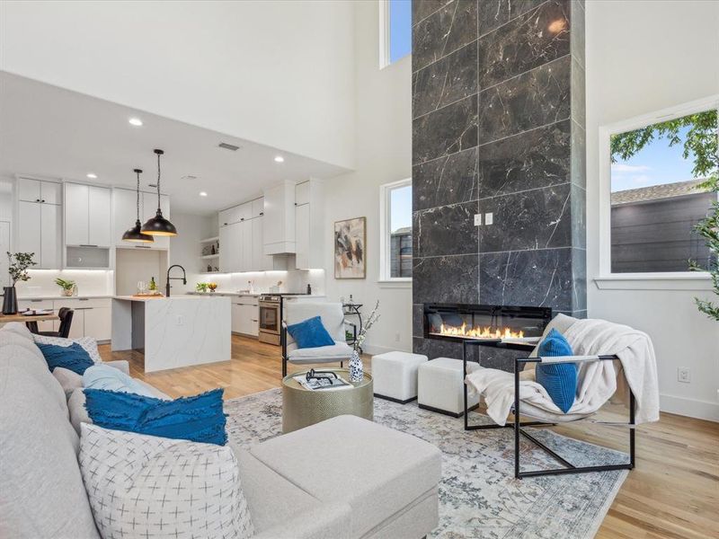 Living room with a towering ceiling, sink, a tiled fireplace, and light wood-type flooring