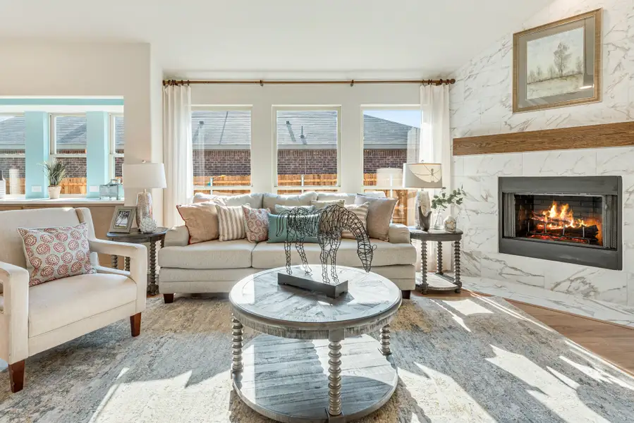 Living room with marble fireplace, neutral sofa, round coffee table, and large windows letting in natural light