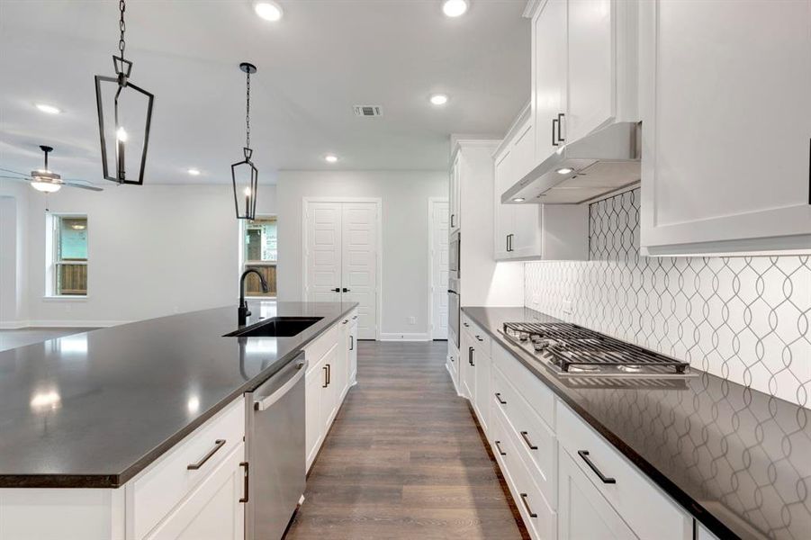 Kitchen featuring white cabinets, stainless steel appliances, dark wood finished floors, dark stone counters, and decorative light fixtures