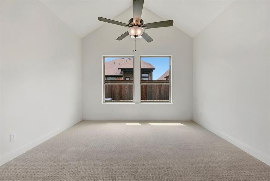 Vaulted ceiling room featuring two windows, neutral tone carpeting, and a ceiling fan with integrated lighting
