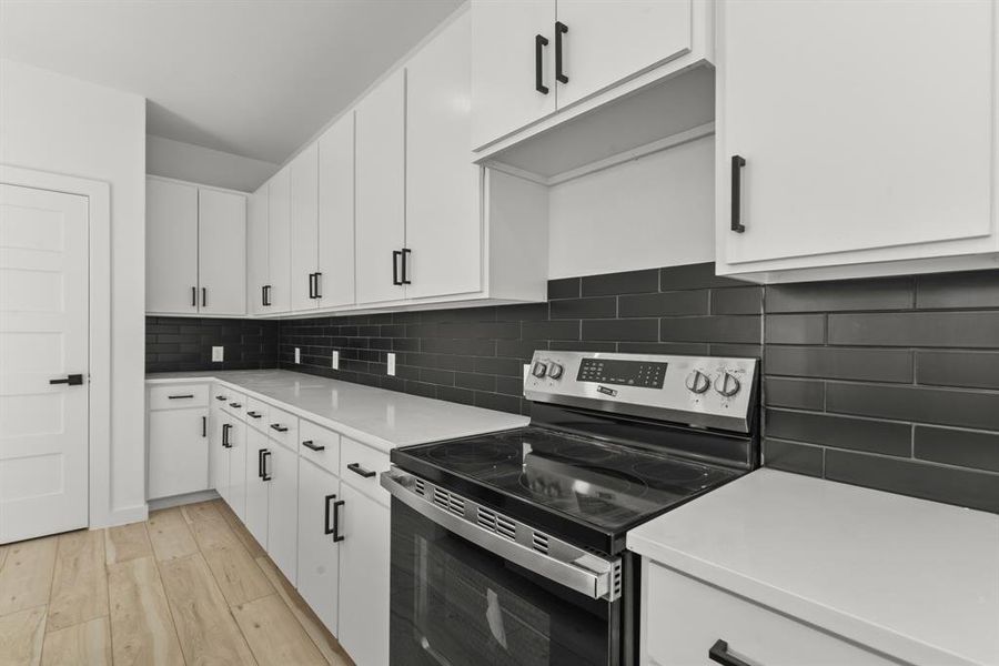 Kitchen featuring light wood finished floors, white cabinets, decorative backsplash, stainless steel electric range oven, and light countertops