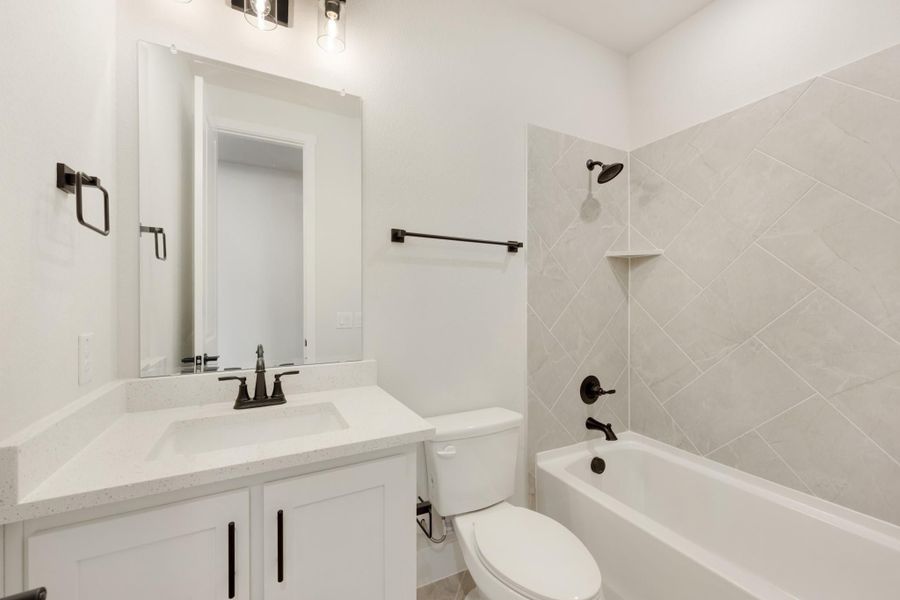 Bathroom with white vanity, quartz countertop, tub-shower combo with diagonal tile, and dark bronze fixtures