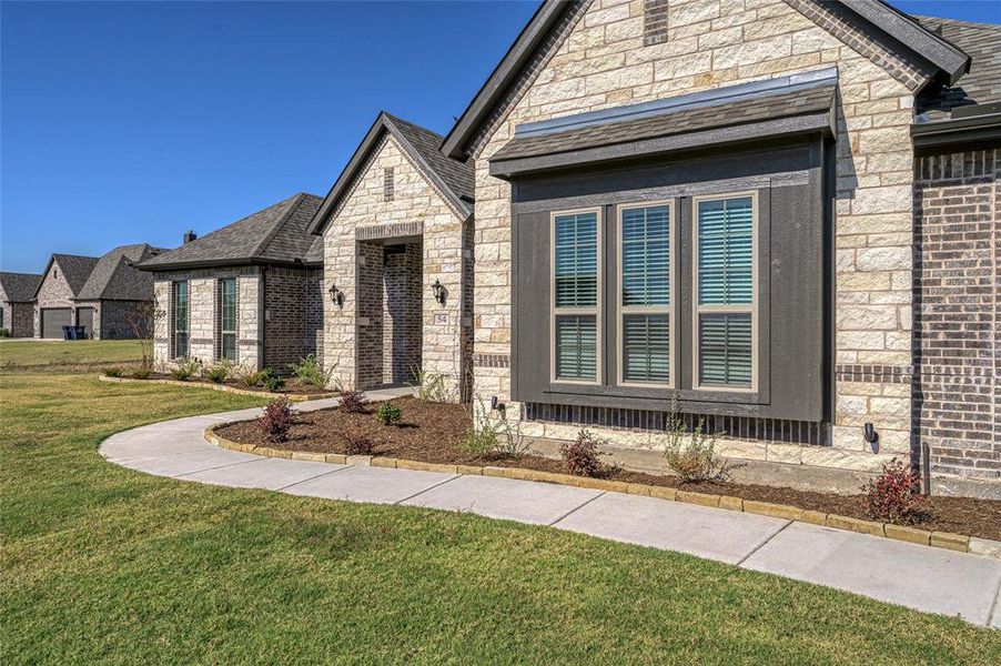 French country style house with a front lawn, brick siding, stone siding, and a shingled roof