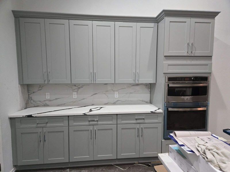 Kitchen featuring stainless steel double oven, gray cabinets, light stone countertops, and backsplash