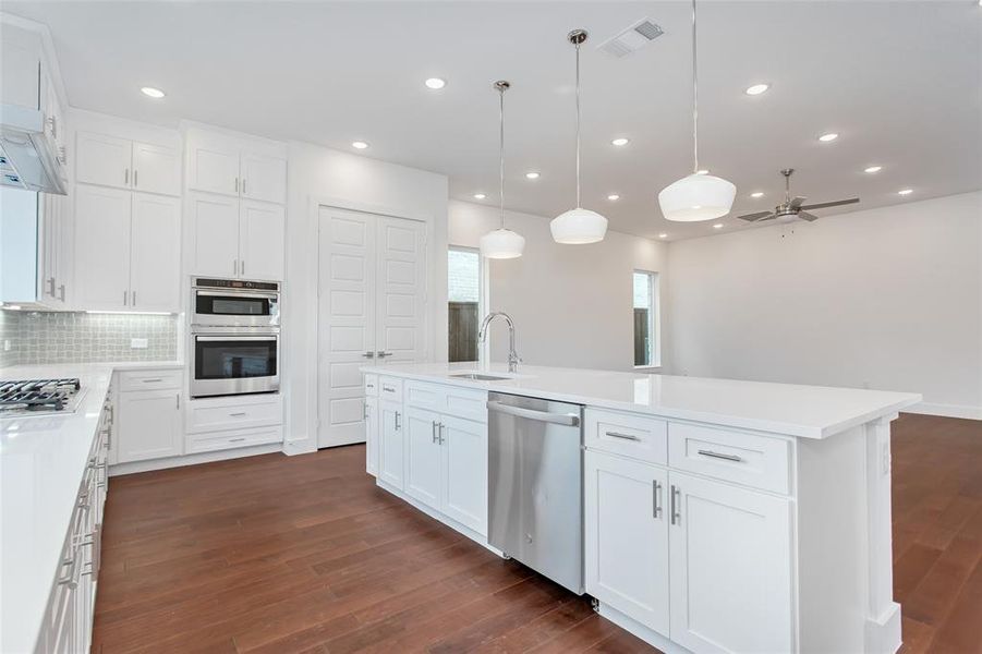 Kitchen with stainless steel appliances, hanging light fixtures, decorative backsplash, an island with sink, and dark wood-type flooring