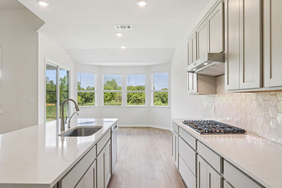 Kitchen with light stone counters, light wood-style flooring, an island with sink, recessed lighting, and backsplash Kitchen with light stone counters, light wood-style flooring, an island with sink, recessed lighting, and backsplash