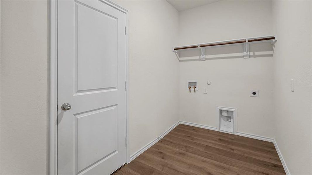 Dedicated laundry space featuring a white door, light-colored walls, and durable flooring, complete with an overhead shelf for storage