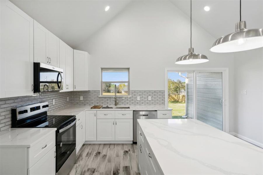 Kitchen featuring high vaulted ceiling, white cabinets, decorative backsplash, decorative light fixtures, and stainless steel appliances