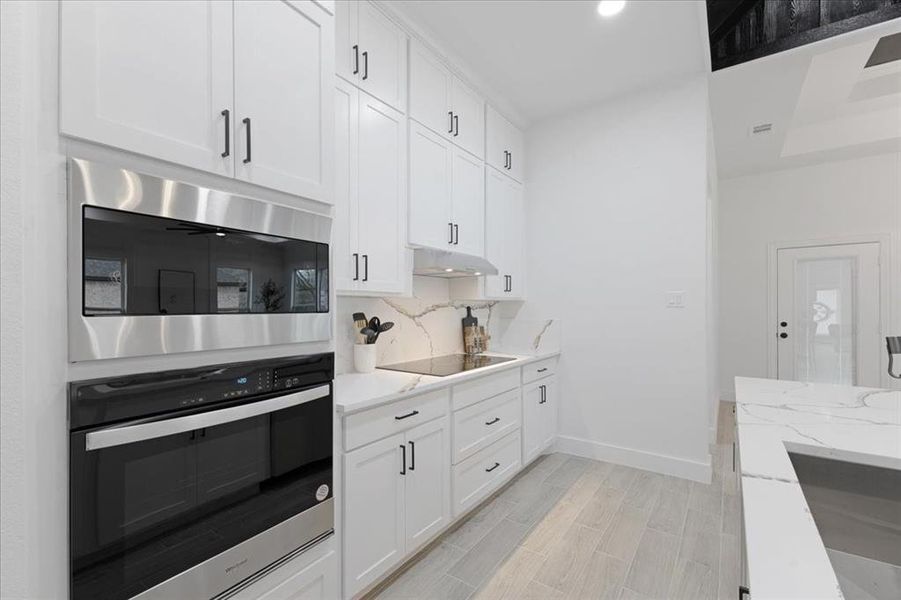 Kitchen with black appliances, light stone countertops, white cabinets, and under cabinet range hood