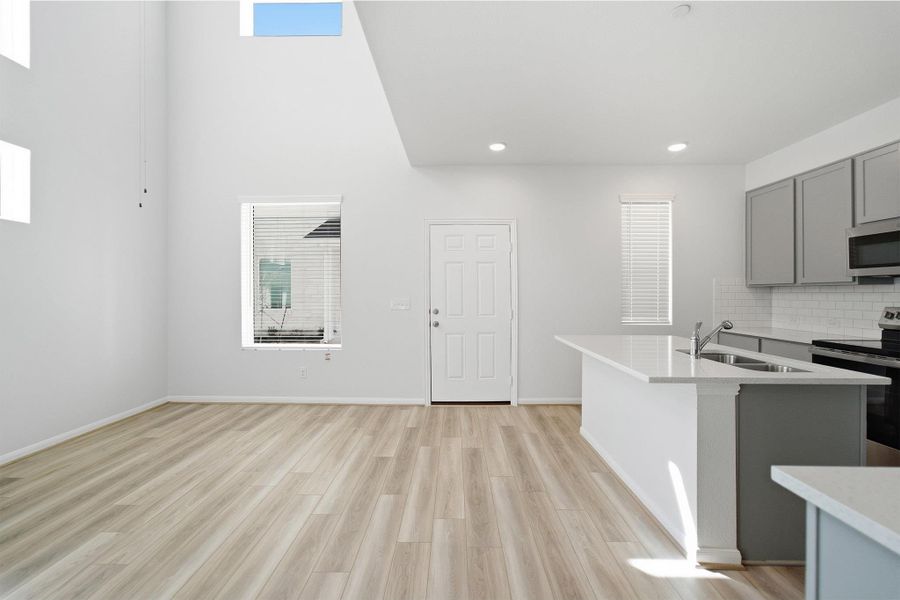Kitchen with gray cabinets, stainless steel appliances, a kitchen island with sink, light wood-type flooring, and light stone countertops