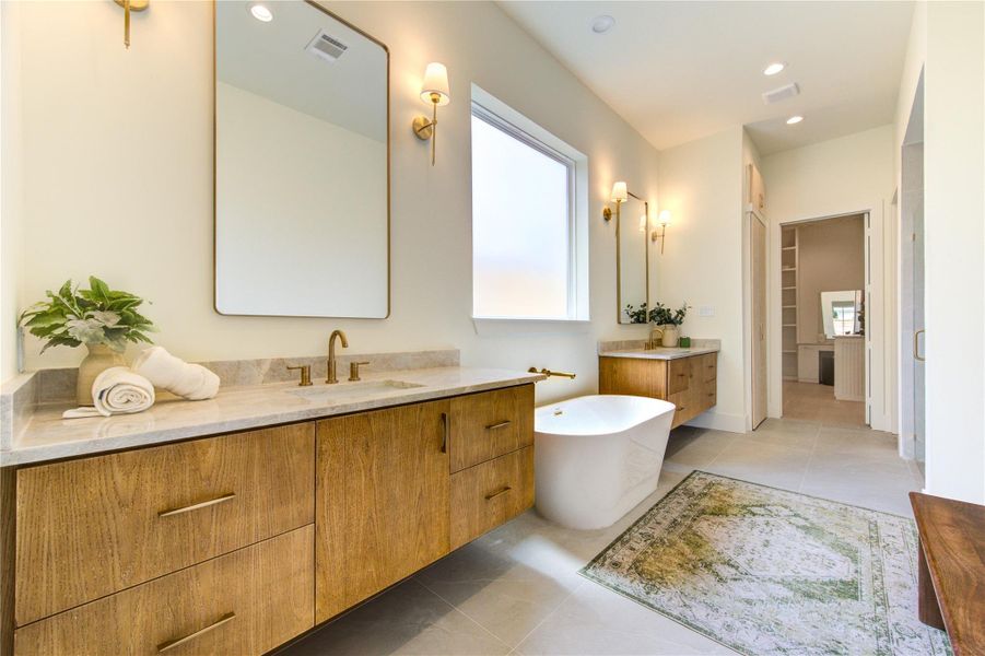 The spa-inspired primary bath showcases dual furniture-style vanities, luxurious stone surfaces, designer lighting, and a freestanding soaking tub.