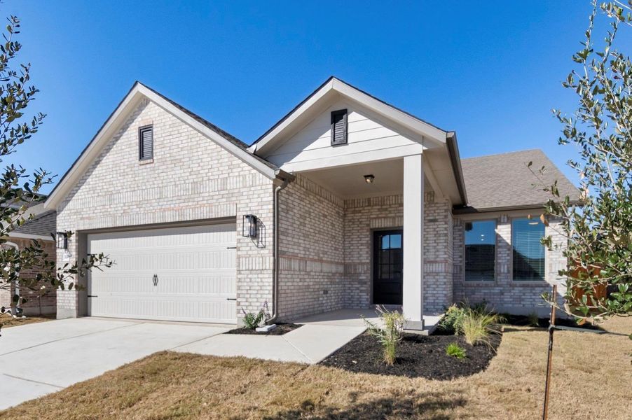 View of front of house with brick siding, driveway, an attached garage, a front yard, and a porch