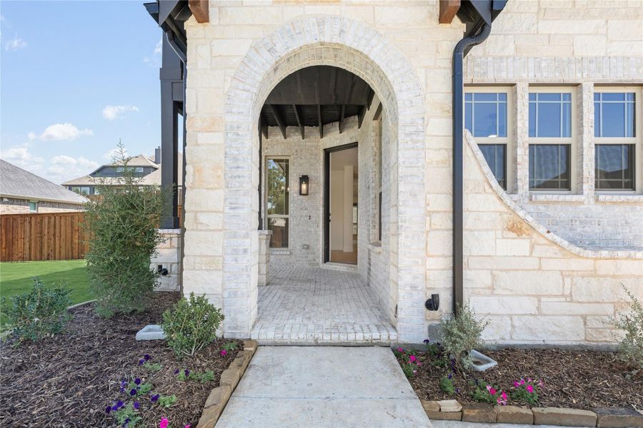 Stone home entrance with arched brick doorway, covered porch, and landscaped walkway with flowers Stone home entrance with arched brick doorway, covered porch, and landscaped walkway with flowers