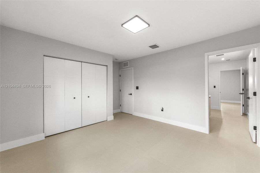 Neutral-toned room featuring large-format tile flooring, recessed square ceiling lighting, white flush-panel closet doors, and matte black door hardware