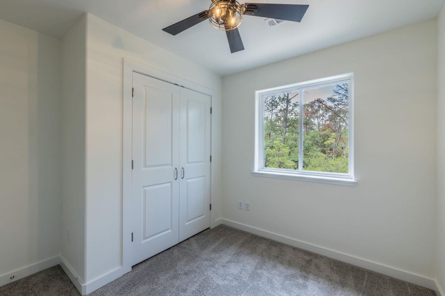 Bedroom featuring neutral wall paint, gray carpet flooring, a double-door closet, and a white-framed window Bedroom featuring neutral wall paint, gray carpet flooring, a double-door closet, and a white-framed window