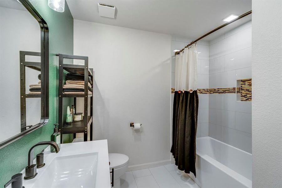 Full bathroom with toilet, sink, tile patterned floors, and shower / bath combo with shower curtain