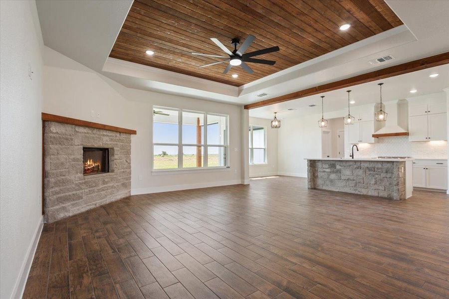 An inviting great room boasts a stone fireplace, wood-look tile flooring, and a unique wood plank ceiling with recessed lighting.