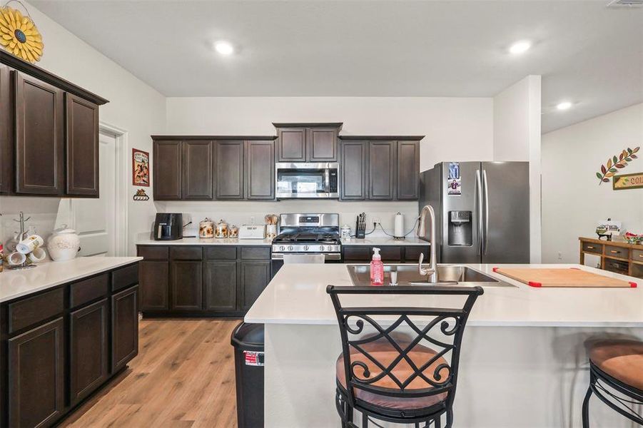 Kitchen featuring a breakfast bar area, appliances with stainless steel finishes, dark brown cabinetry, light wood-type flooring, and a kitchen island with sink